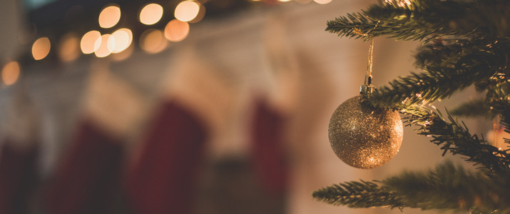 Närbild av en guldig julgranskula som hänger på en julgran. I bakgrunden syns julstrumpor.