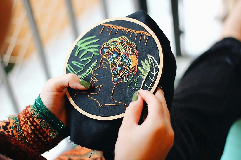En person broderar ett färgglatt mönster på ett svart tygstycke.