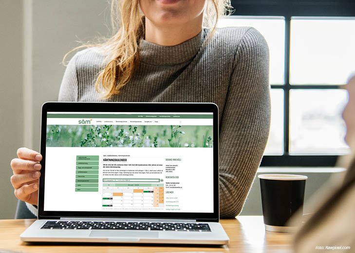 En person med grå tröja och blont hår visar upp en laptop med skärmen mot kameran. På laptopen syns SÅM:s hemsida med hämtningskalendern.