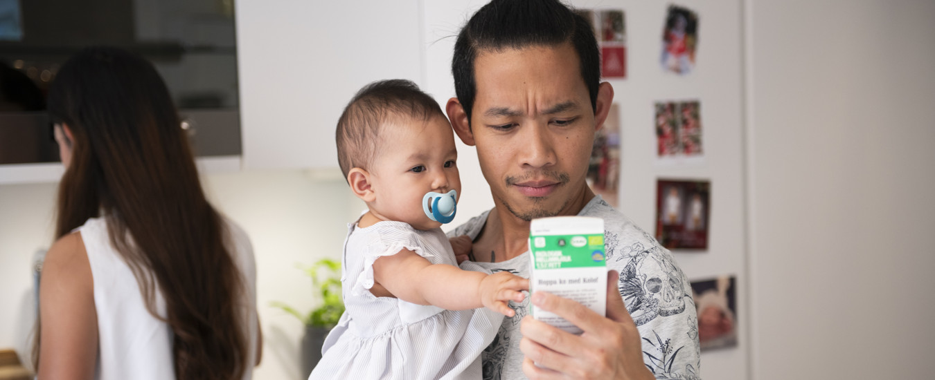 En person med en bebis i famnen tittar på datummärkningen på en mjölkförpackning.