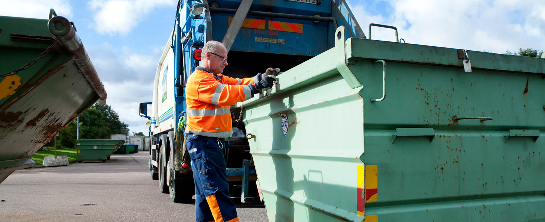 En sopbilschaufför i färd med att tömma en stor grön container med avfall.