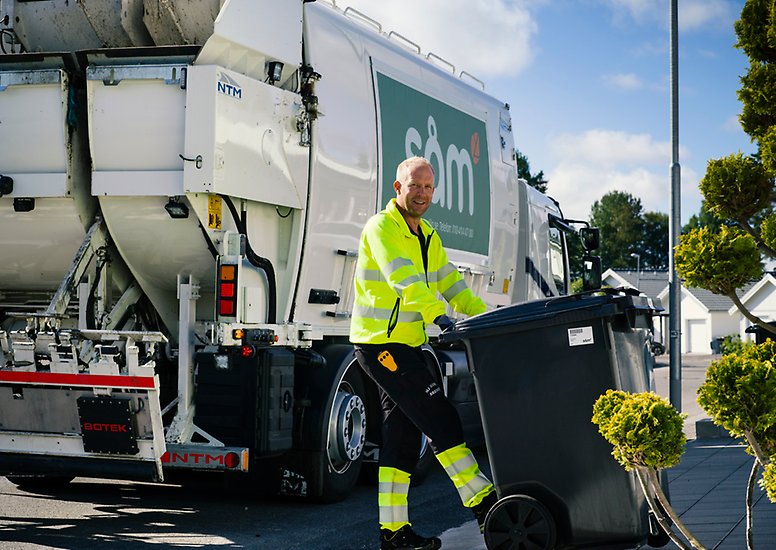 En man iklädd varseljacka fäster ett fyrfackskärl på sopbilen för tömning.