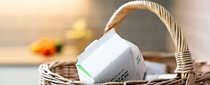 Närbild av en mjölkförpackning i en flätad korg för återvinning.