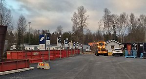 Översikt över Smålandsstenars återvinningscentral. Till vänster syns röda containrar med tydliga skyltar för varje fraktion. Till höger syns en hjullastare.