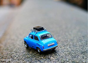 Blå leksaksbil av äldre modell med en brun koffert på taket.