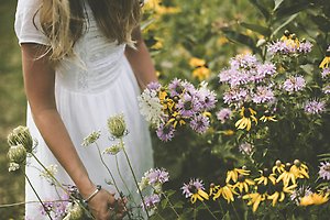 En person i vit klänning vid en blomsteräng.