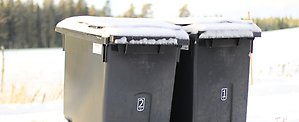 Två mörkgråa avfallskärl i vinterlandskap.